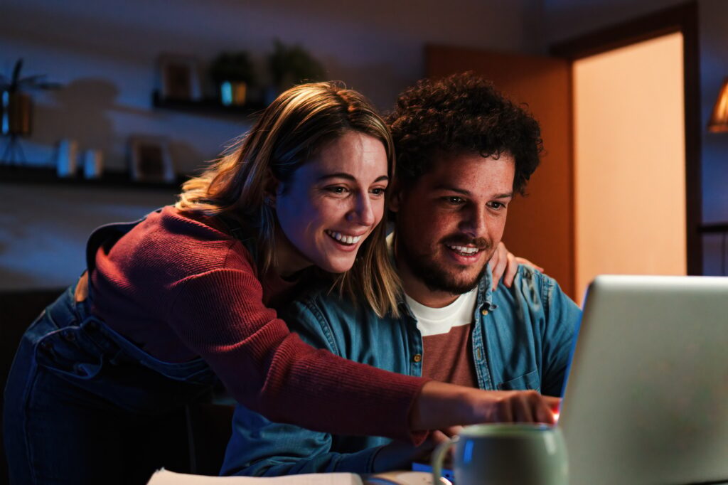 young happy caucasian couple browsing on internet using a laptop to search sale at home excited